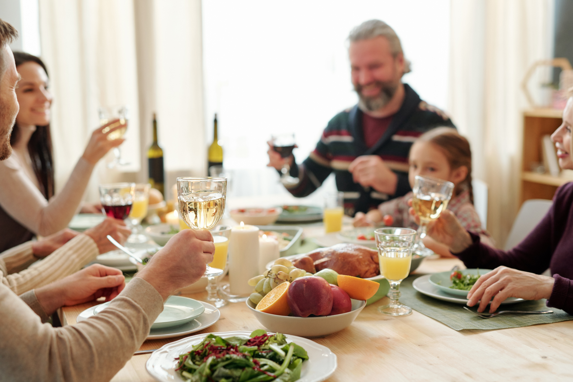 Hand of young man holding glass of wine over served table during toast at festive family dinner on Thanksgiving day